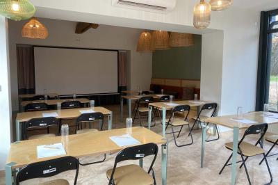 Salle de restaurant lumineuse avec tables dressées, banquettes vertes, chaises blanches et vue sur un jardin arboré.