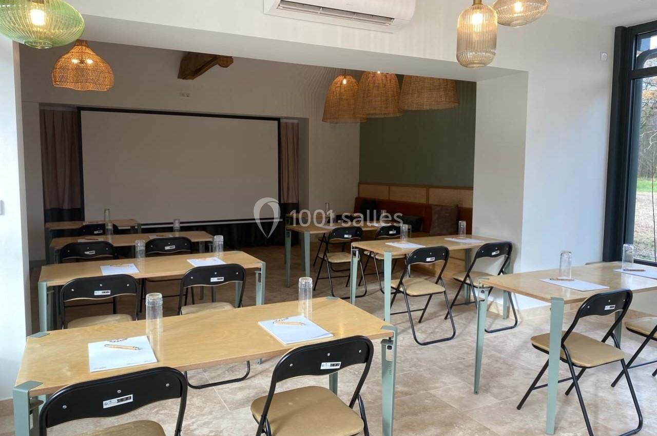 Salle de réunion lumineuse avec tables, chaises pliantes, écran de projection et bouteilles d'eau sur chaque table.