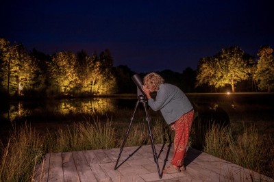 Salle de restaurant lumineuse avec tables dressées, banquettes vertes, chaises blanches et vue sur un jardin arboré.
