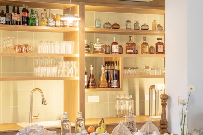 Salle de restaurant lumineuse avec tables dressées, banquettes vertes, chaises blanches et vue sur un jardin arboré.