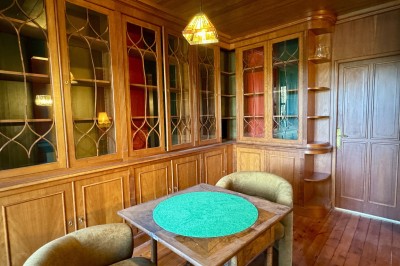 Salle de restaurant lumineuse avec tables dressées, banquettes vertes, chaises blanches et vue sur un jardin arboré.