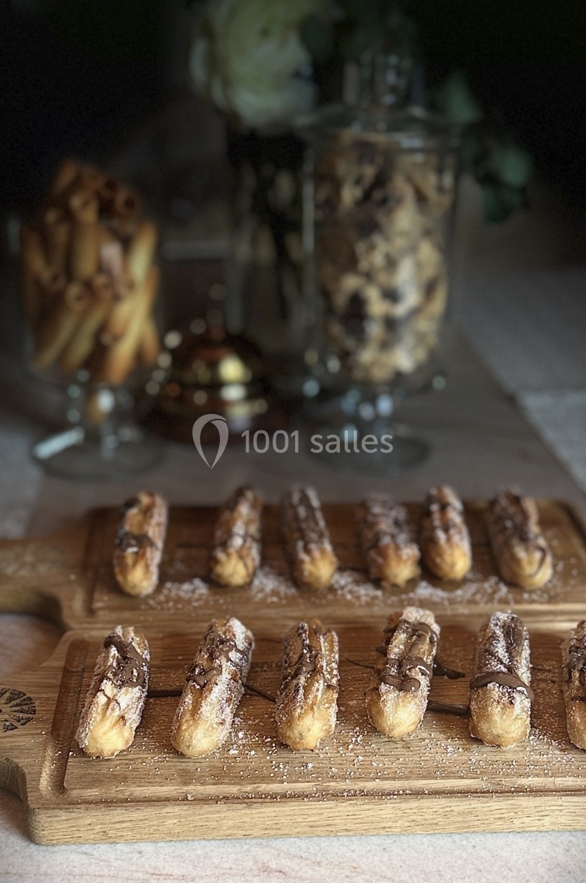 Éclairs au chocolat disposés sur des planches en bois, avec des biscuits et décorations en arrière-plan.