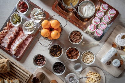 Salle de restaurant lumineuse avec tables dressées, banquettes vertes, chaises blanches et vue sur un jardin arboré.