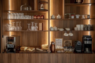 Salle de restaurant lumineuse avec tables dressées, banquettes vertes, chaises blanches et vue sur un jardin arboré.