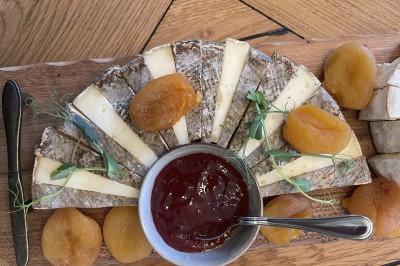 Salle de restaurant lumineuse avec tables dressées, banquettes vertes, chaises blanches et vue sur un jardin arboré.