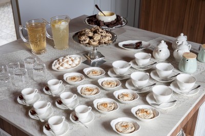 Salle de restaurant lumineuse avec tables dressées, banquettes vertes, chaises blanches et vue sur un jardin arboré.