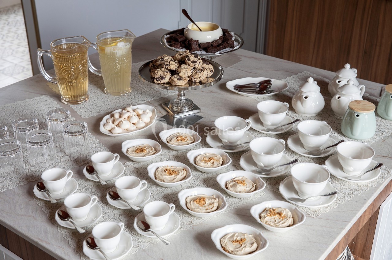 Table dressée avec des tasses, assiettes de desserts, pichets de boissons, théières et plateaux de biscuits.