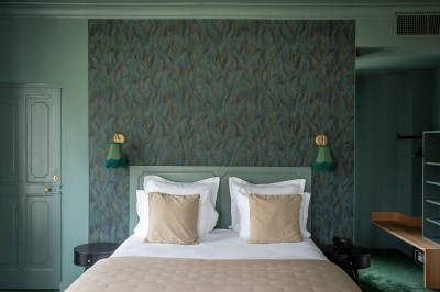 Salle de restaurant lumineuse avec tables dressées, banquettes vertes, chaises blanches et vue sur un jardin arboré.