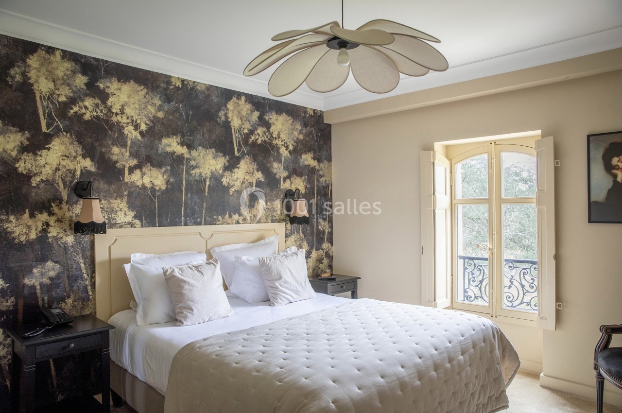 Chambre lumineuse avec lit double, mur décoré de motifs forestiers, fenêtre ouverte sur un balcon en fer forgé.