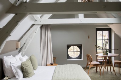 Salle de restaurant lumineuse avec tables dressées, banquettes vertes, chaises blanches et vue sur un jardin arboré.