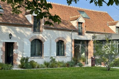 Salle de restaurant lumineuse avec tables dressées, banquettes vertes, chaises blanches et vue sur un jardin arboré.