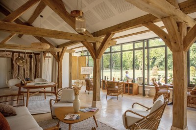 Salle de restaurant lumineuse avec tables dressées, banquettes vertes, chaises blanches et vue sur un jardin arboré.
