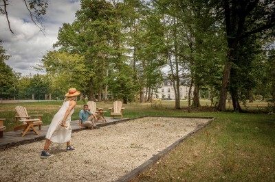 Salle de restaurant lumineuse avec tables dressées, banquettes vertes, chaises blanches et vue sur un jardin arboré.