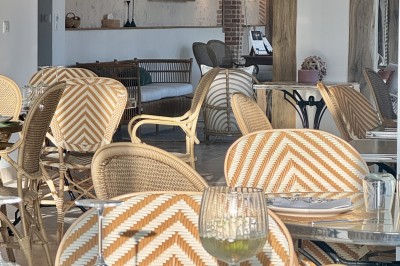 Salle de restaurant lumineuse avec tables dressées, banquettes vertes, chaises blanches et vue sur un jardin arboré.