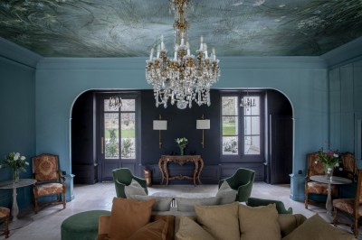 Salle de restaurant lumineuse avec tables dressées, banquettes vertes, chaises blanches et vue sur un jardin arboré.