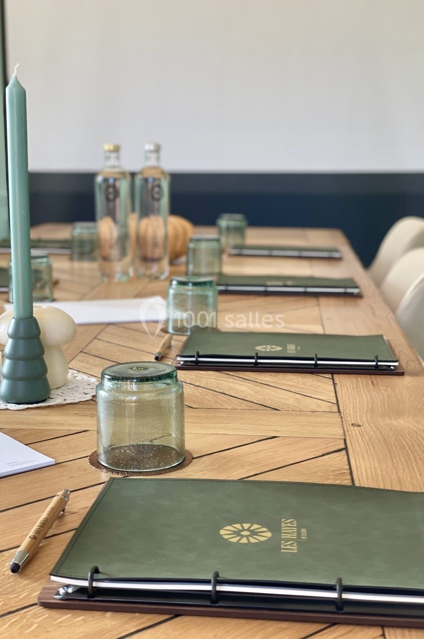 Table en bois avec carnets, stylos, bougies vertes et bouteilles d'eau, préparée pour une réunion ou un atelier.