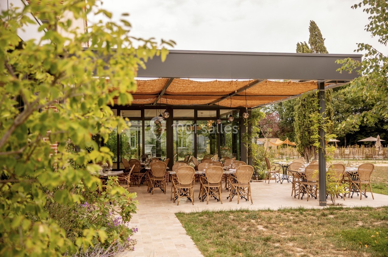 Terrasse d'un restaurant avec des tables et chaises en rotin, abritée par une pergola, entourée de végétation.