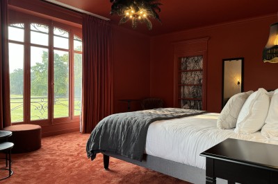 Salle de restaurant lumineuse avec tables dressées, banquettes vertes, chaises blanches et vue sur un jardin arboré.