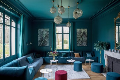 Salle de restaurant lumineuse avec tables dressées, banquettes vertes, chaises blanches et vue sur un jardin arboré.