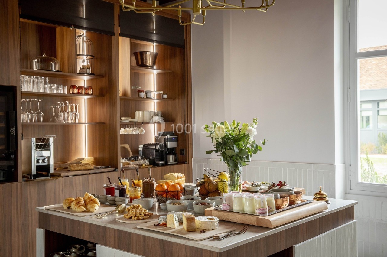 Buffet de petit-déjeuner avec viennoiseries, fruits, fromages, yaourts et boissons, disposé sur une table en bois.