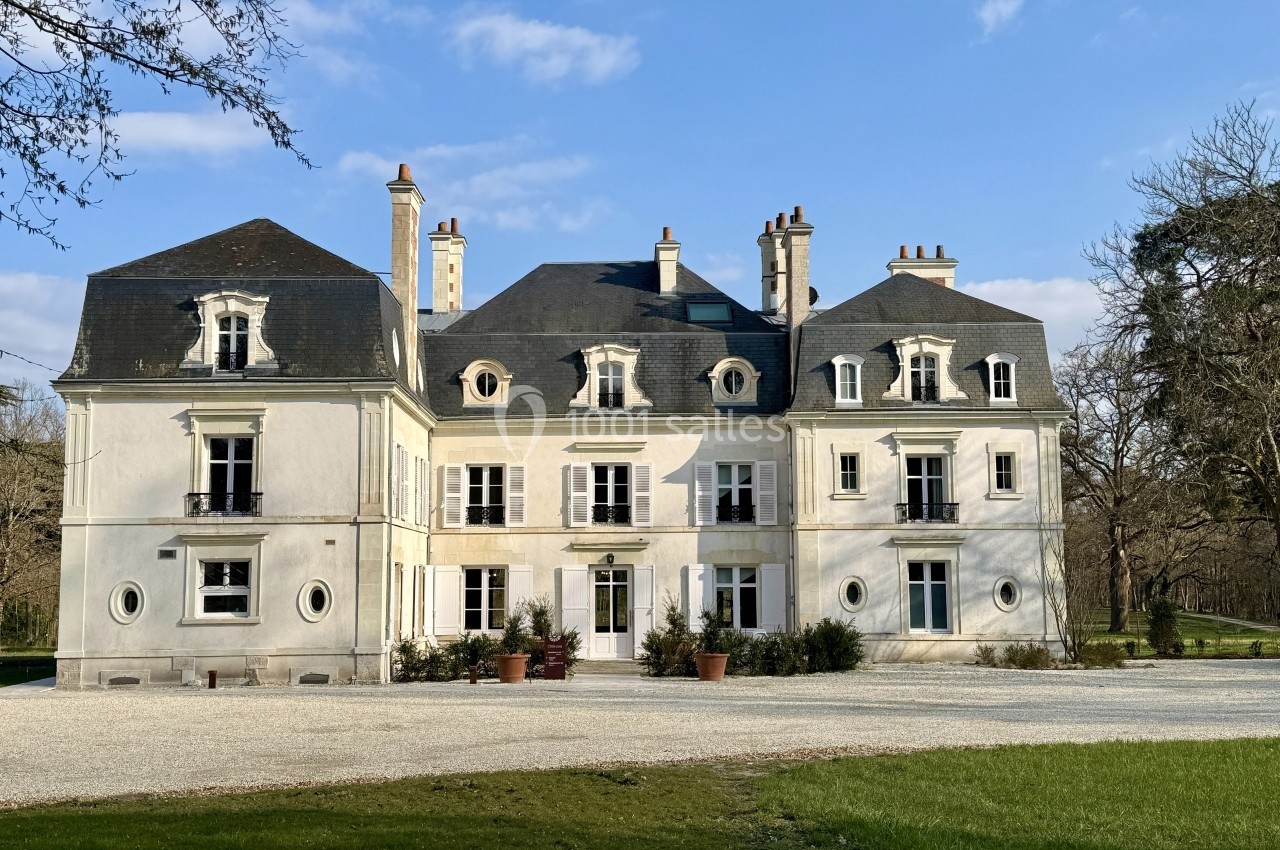 Façade d'un château blanc à deux étages avec toit en ardoise, entouré d'arbres et d'une allée gravillonnée.