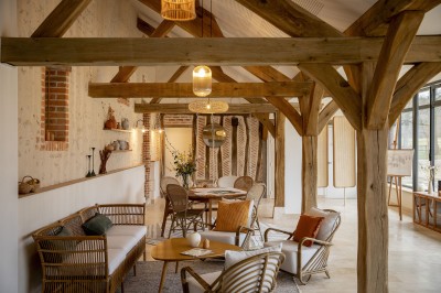 Salle de restaurant lumineuse avec tables dressées, banquettes vertes, chaises blanches et vue sur un jardin arboré.