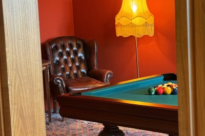Salle de restaurant lumineuse avec tables dressées, banquettes vertes, chaises blanches et vue sur un jardin arboré.