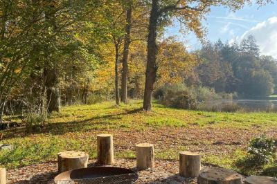 Vue aérienne d'un terrain de tennis rouge entouré de forêt, avec une petite mare et des prairies avoisinantes.