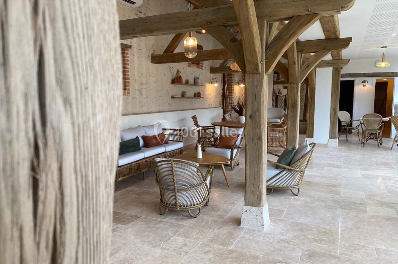 Espace intérieur lumineux avec poutres en bois, mobilier en rotin et sol en pierre claire.