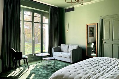 Vue aérienne d'un terrain de tennis rouge entouré de forêt, avec une petite mare et des prairies avoisinantes.