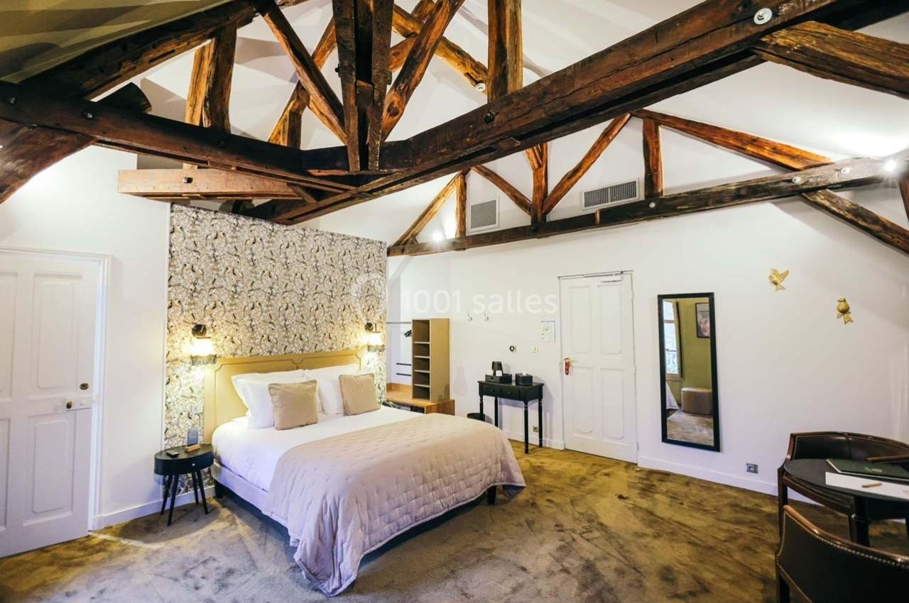 Chambre lumineuse avec poutres apparentes, lit double, bureau, chaises et décoration murale dans un style chaleureux.