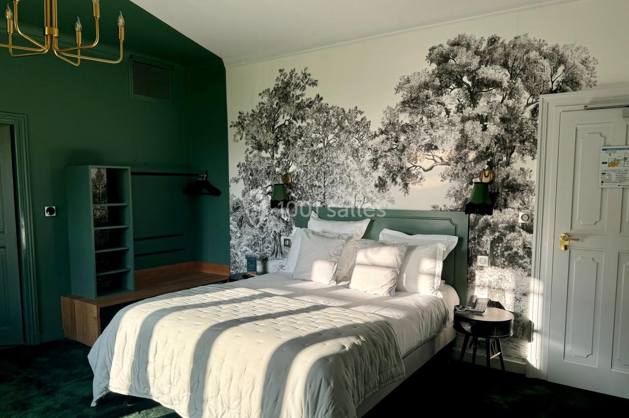 Chambre lumineuse avec lit double, mur vert, fresque d'arbres en noir et blanc, et mobilier minimaliste.