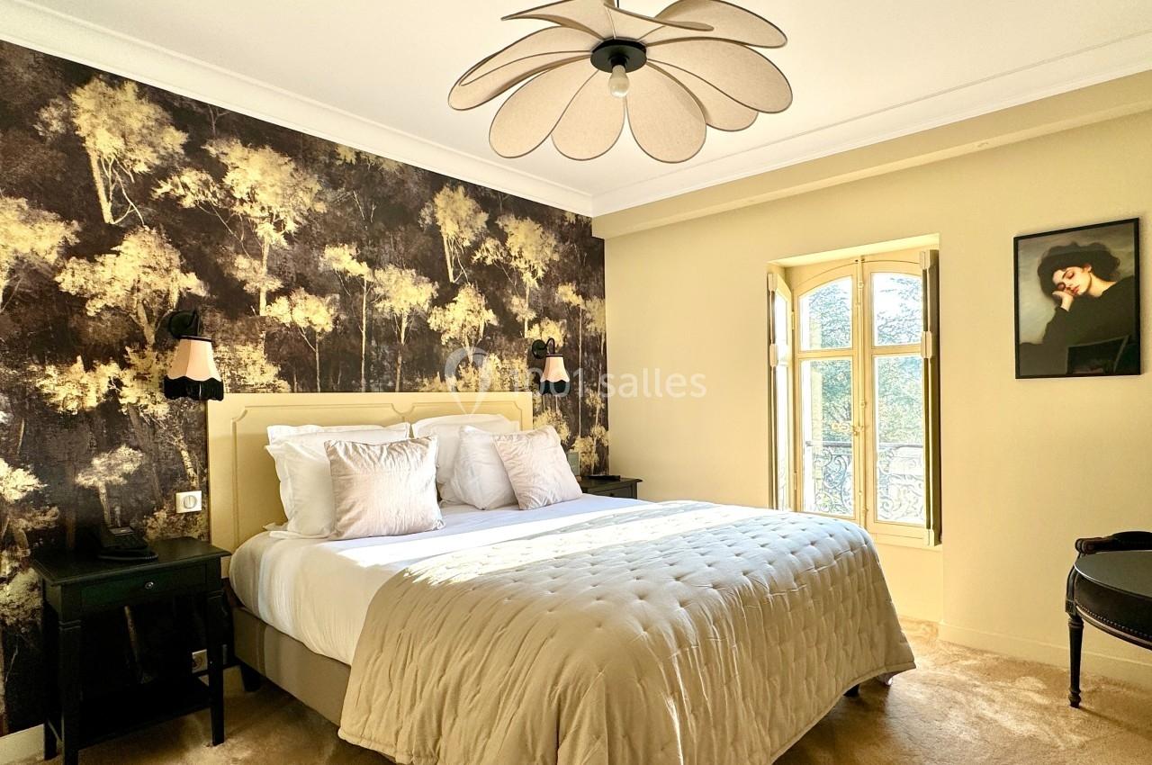 Chambre lumineuse avec lit double, mur décoré d'un papier peint nature, et fenêtre à double battant.