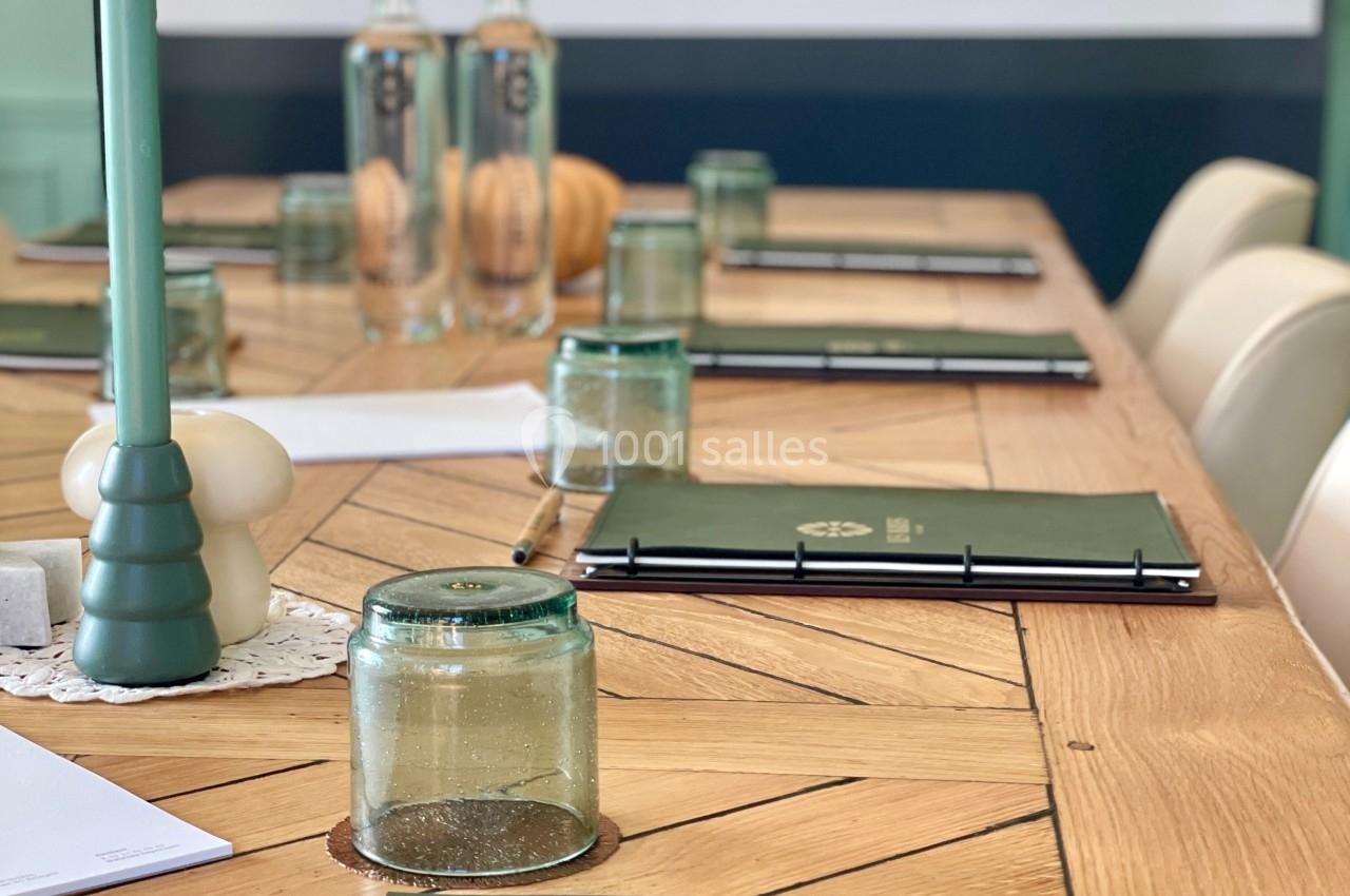 Table en bois avec carnets, stylos, bougies et bouteilles d'eau, disposés pour une réunion ou un atelier.