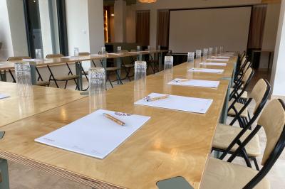 Vue aérienne d'un terrain de tennis rouge entouré de forêt, avec une petite mare et des prairies avoisinantes.