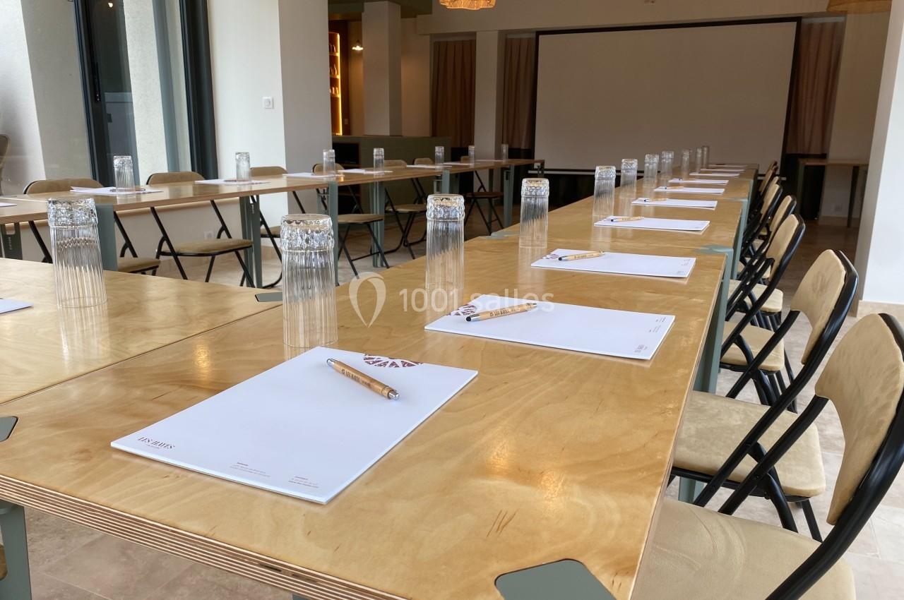 Salle de réunion avec tables en bois alignées, chaises pliantes, blocs-notes, crayons et verres d'eau disposés.