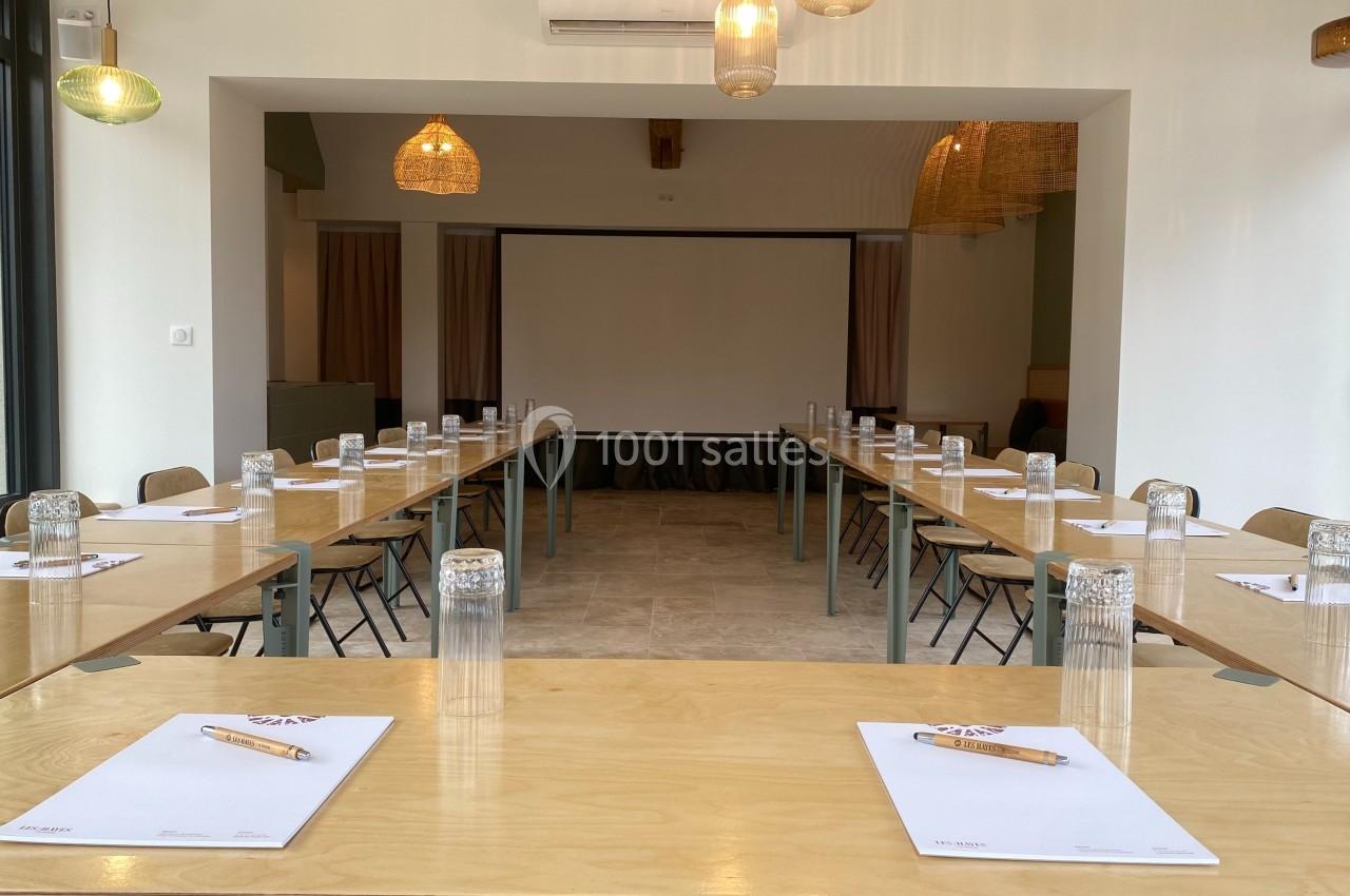 Salle de réunion lumineuse avec tables disposées en U, blocs-notes, crayons et verres d'eau prêts pour les participants.