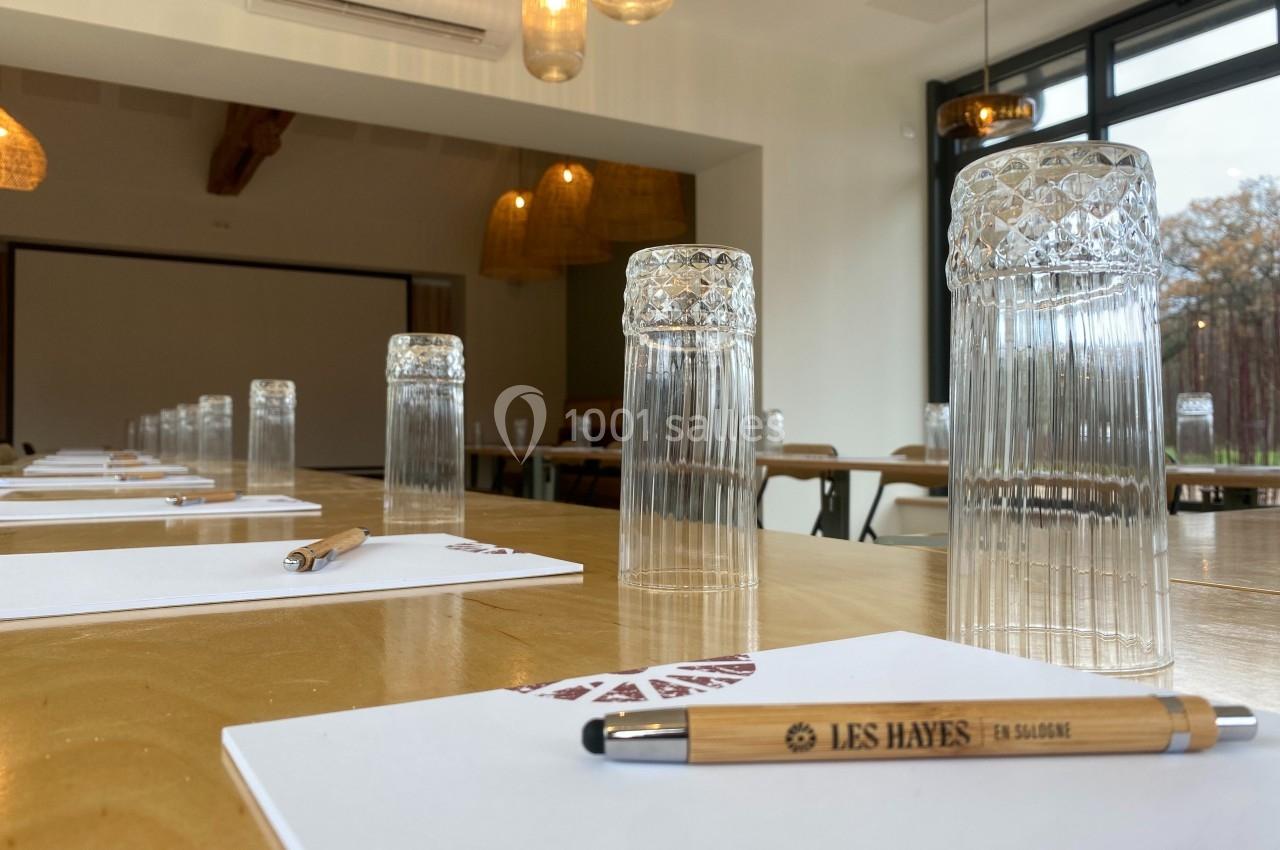 Salle de réunion lumineuse avec des verres empilés, des stylos et des blocs-notes disposés sur une table en bois.