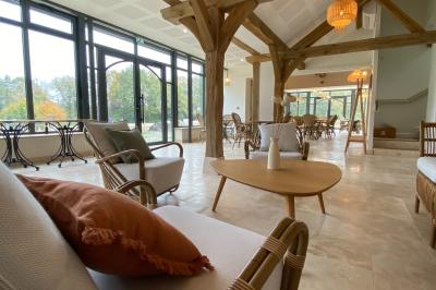 Vue aérienne d'un terrain de tennis rouge entouré de forêt, avec une petite mare et des prairies avoisinantes.