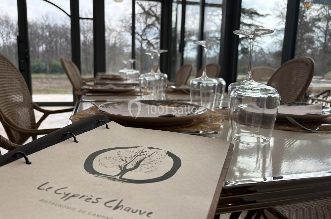 Salle de restaurant lumineuse avec des tables dressées, vue sur un extérieur arboré à travers de grandes baies vitrées.