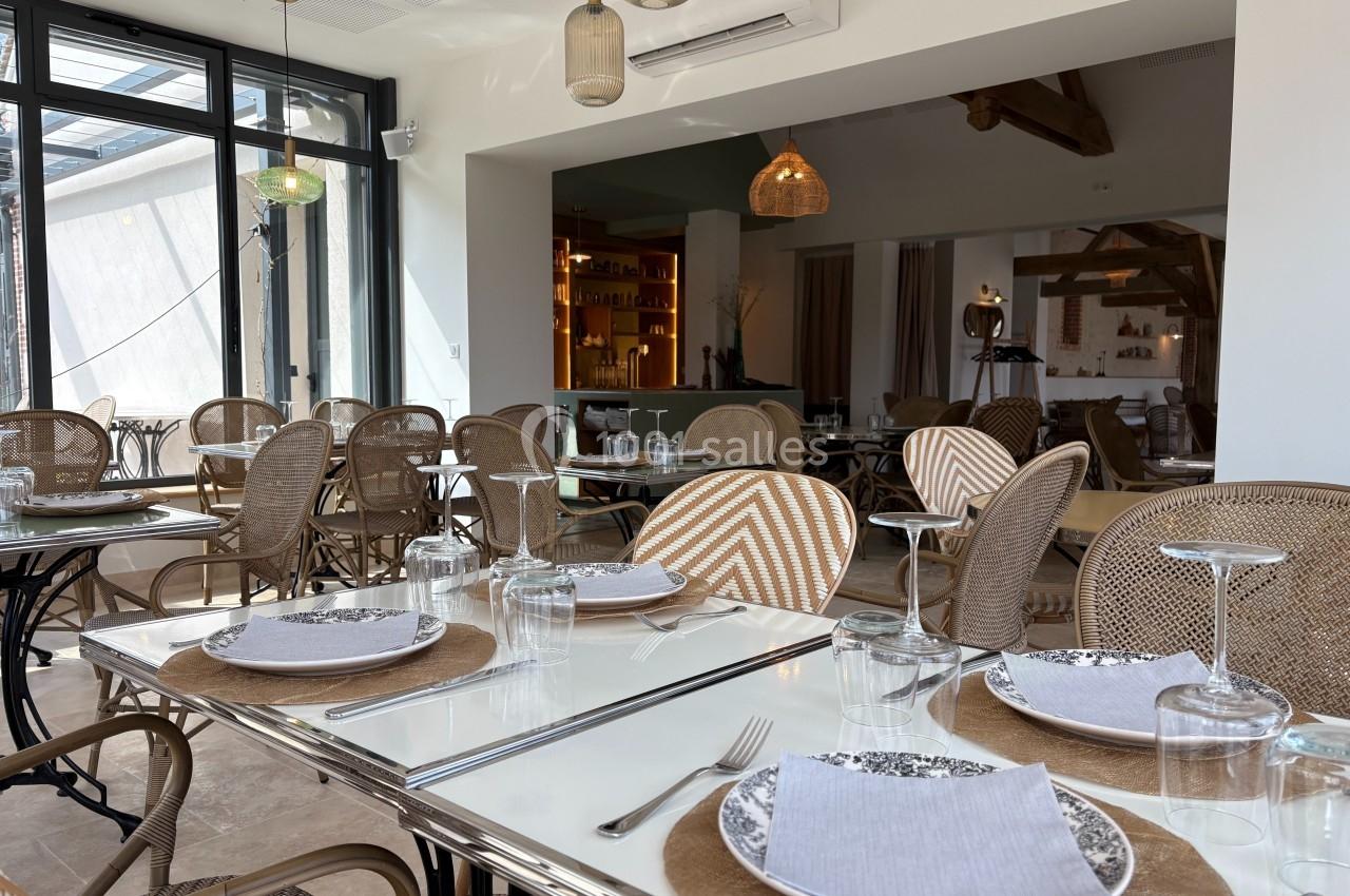 Salle de restaurant lumineuse avec tables dressées, chaises en rotin et décoration intérieure chaleureuse.