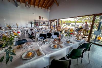Terrasse en bois avec tables, bancs et grande baie vitrée donnant sur un espace extérieur avec quelques bâtiments au loin.