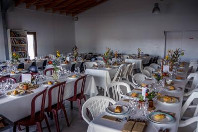 Terrasse en bois avec tables, bancs et grande baie vitrée donnant sur un espace extérieur avec quelques bâtiments au loin.