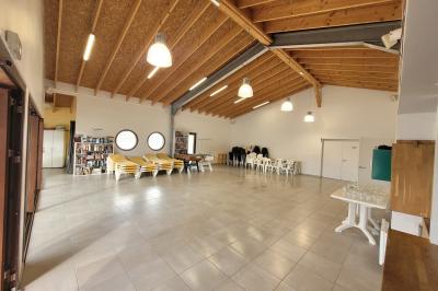 Terrasse en bois avec tables, bancs et grande baie vitrée donnant sur un espace extérieur avec quelques bâtiments au loin.