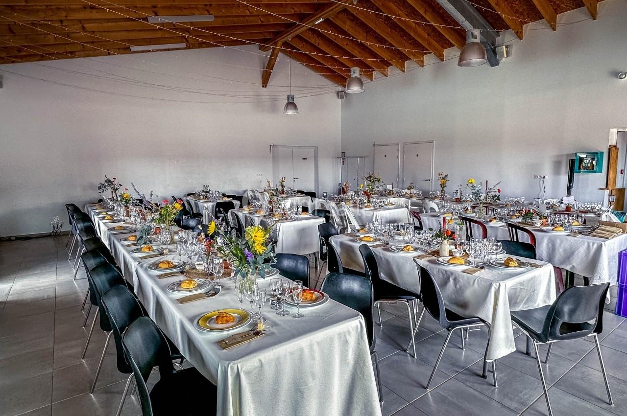 Salle de réception décorée avec des tables dressées, nappes blanches, chaises noires et arrangements floraux colorés.