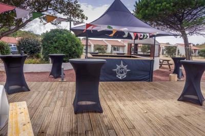 Terrasse en bois avec tables, bancs et grande baie vitrée donnant sur un espace extérieur avec quelques bâtiments au loin.