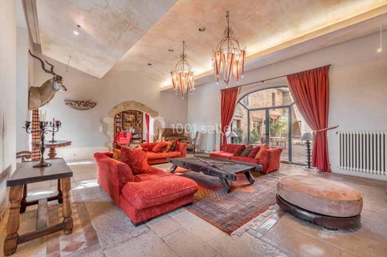 Salon spacieux avec canapés rouges, table basse en bois, lustres suspendus et grande baie vitrée donnant sur l'extérieur.