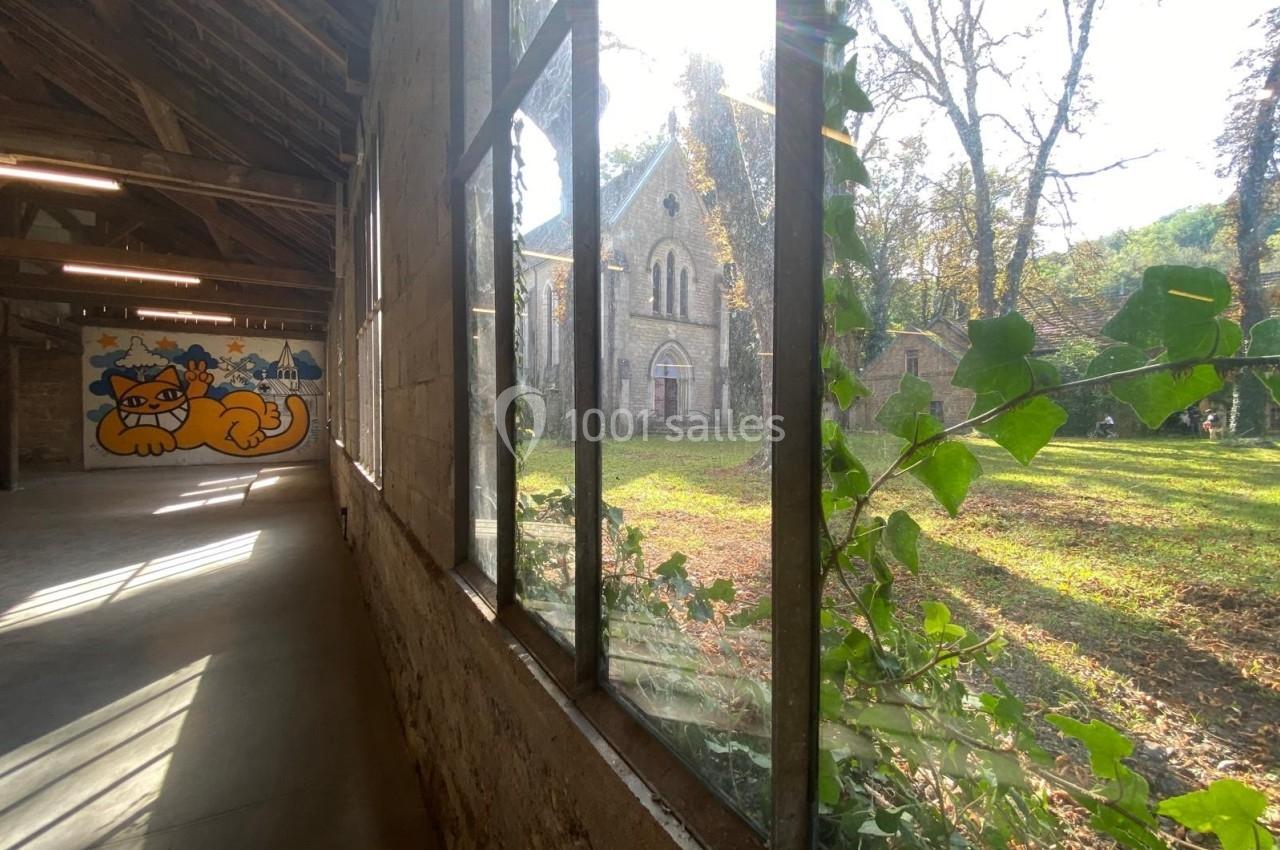 Vue d'une chapelle ancienne à travers une fenêtre, avec lierre grimpant et fresque murale d'un chat à gauche.