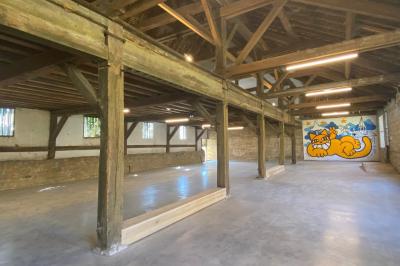 Miniature Location salle Toulouse-le-Château (Jura) - Forges de Baudin #2 Intérieur d'une grande pièce en pierre avec plafond en poutres apparentes, sol en dalles et lumière naturelle.