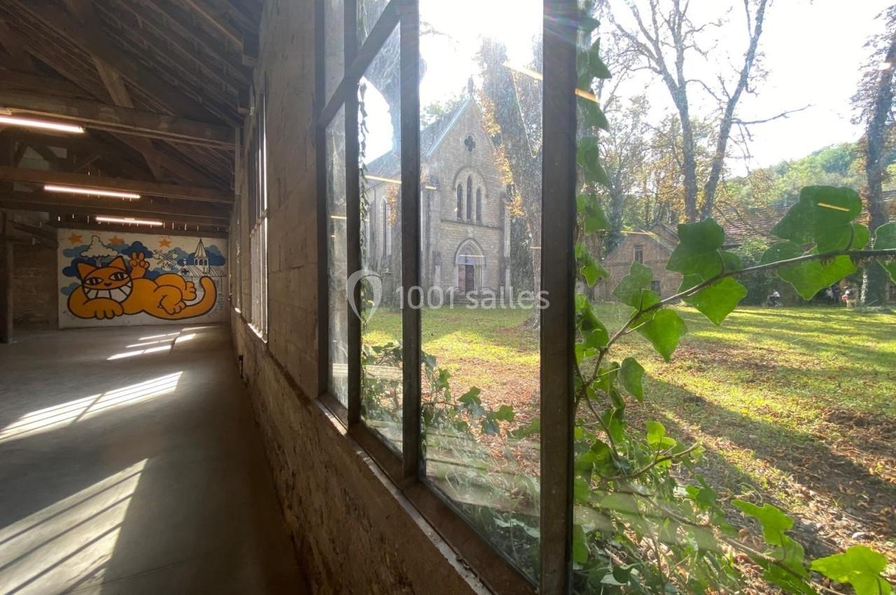 Vue depuis l'intérieur d'un bâtiment avec une fresque de chat, donnant sur un jardin et une église en arrière-plan.